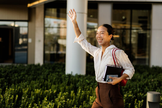 Korean woman joyfully greets friends while walking through a sunny urban area