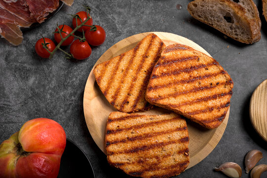 Toasted bread slices with cured Spanish ham, fresh tomatoes, and grated tomato sauce on dark surface, traditional healthy Mediterranean breakfast
