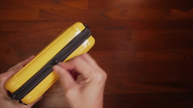 Top view on left side with copy space of woman hands holding yellow bag on wooden table, repeatedly pulling jammed zipper, failure concept.⁠