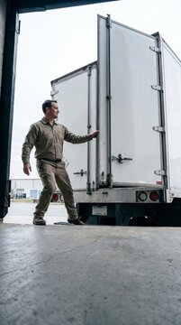 Solitary worker walking beside open trailer doors at industrial warehouse loading entrance