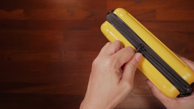 ⁠Top view on right side of woman hands holding yellow pouch on wooden desk, pulling stuck zipper halfway, obstacle concept.⁠