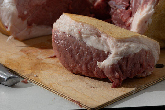 Raw pork leg deboning in home kitchen: close-up of bone-in cut on cutting board
