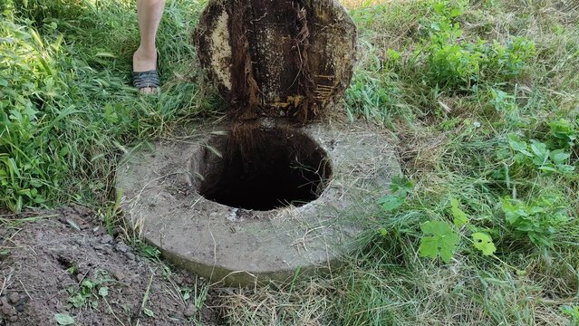 Person in orange gloves holding open septic tank manhole, closing it and walking away