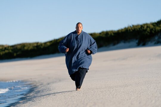 Runner on empty beach wearing roomy blue coat for active lifestyle background and coastal fitness banner
