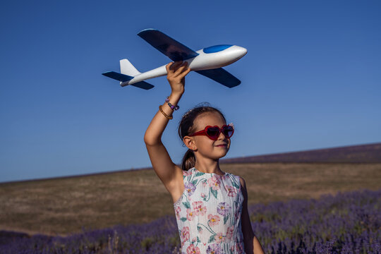 Girl airplane dreams, happy child holding toy glider in lavender field under bright summer sky
