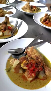 Vertical pan over dozens of plated traditional Indonesian chicken curry dishes ready for catering service in commercial kitchen