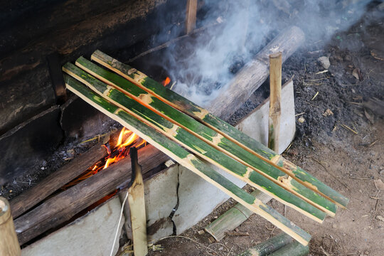 Bamboo strip over campfire with smoke and orange flame in rustic outdoor shelter