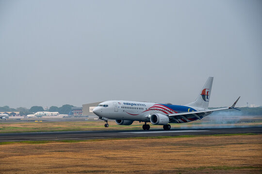 Tangerang, Indonesia - August 22, 2026: Malaysia Airlines Boeing 737 MAX 8 touches down with tire smoke under a hazy sky at Soekarno-Hatta International Airport.