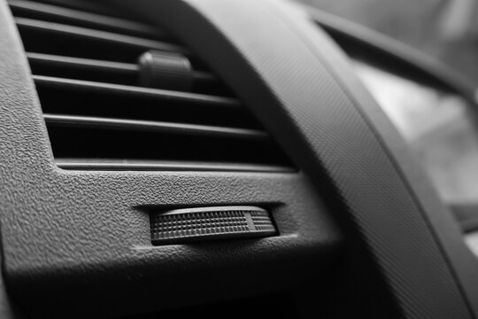 Car dashboard air vent and textured trim in close up, showing black interior detail, control slider, curved surface, and modern vehicle design