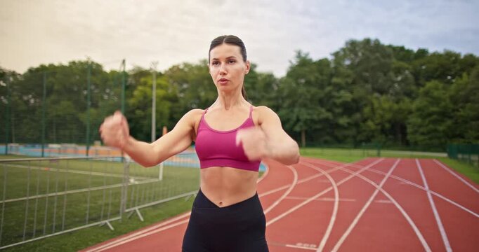 Young athletic woman in sportswear warming up and doing exercises on the stadium running track in the evening at sunset