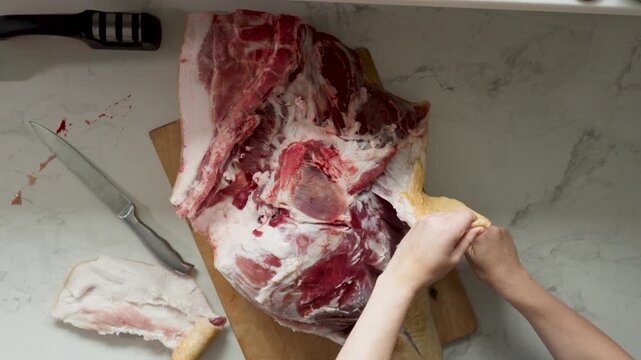 Hands slice and trim raw pork on cutting board during home meat preparation and portioning
