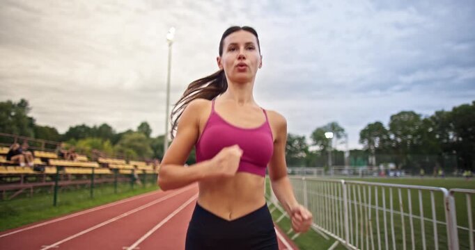 Young athletic woman in sportswear warming up and doing exercises on the stadium running track in the evening at sunset