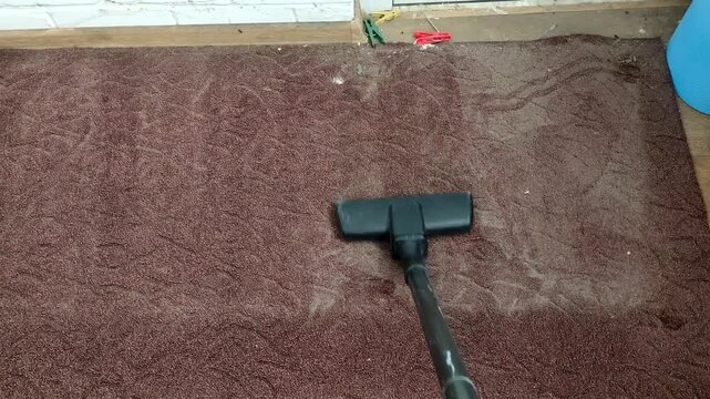 Person vacuuming old brown rug with a vacuum cleaner, first person view