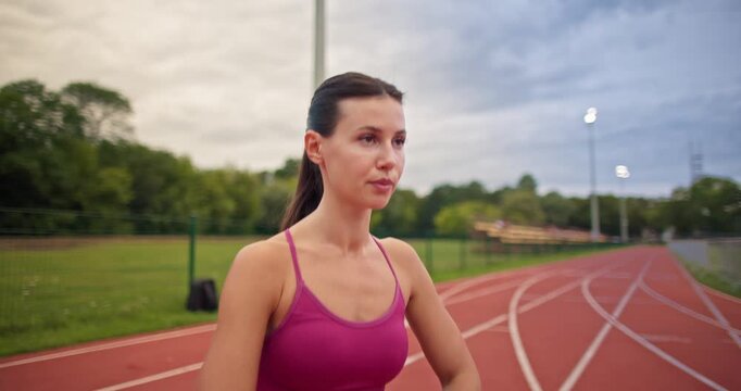 Young athletic woman in sportswear warming up and doing exercises on the stadium running track in the evening at sunset