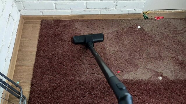 Person vacuuming old and dirty brown rug with a vacuum cleaner, first person view