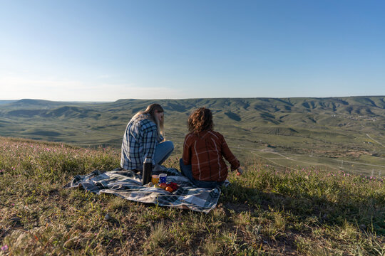 Picnic, women, landscape sitting on blanket on mountain peak enjoying panoramic nature view during summer sunny day with copy space