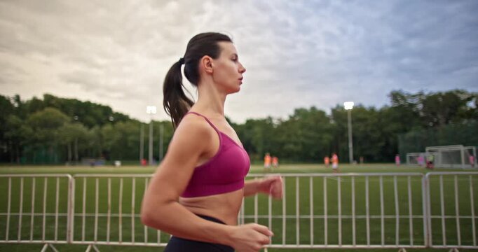 Young athletic woman in sportswear warming up and doing exercises on the stadium running track in the evening at sunset