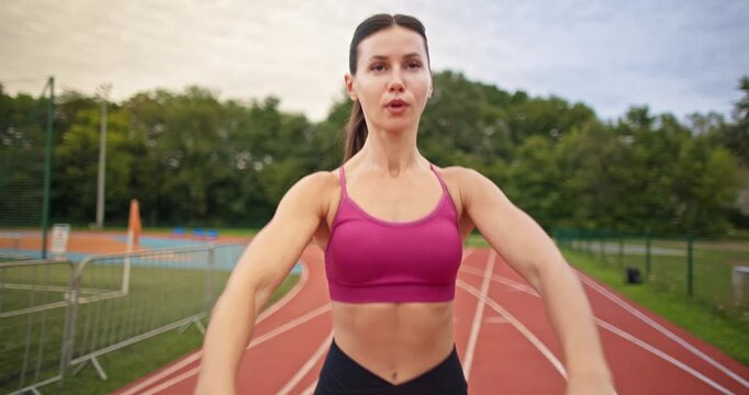 Young athletic woman in sportswear warming up and doing exercises on the stadium running track in the evening at sunset