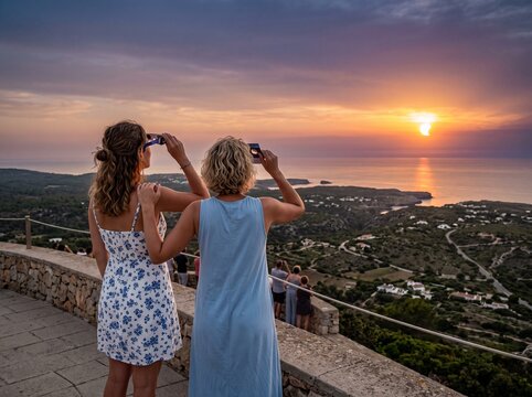 Two women friends in summer dresses looking at a spectacular partial solar eclipse at sunset from Monte Toro viewpoint in Menorca, Spain, back view