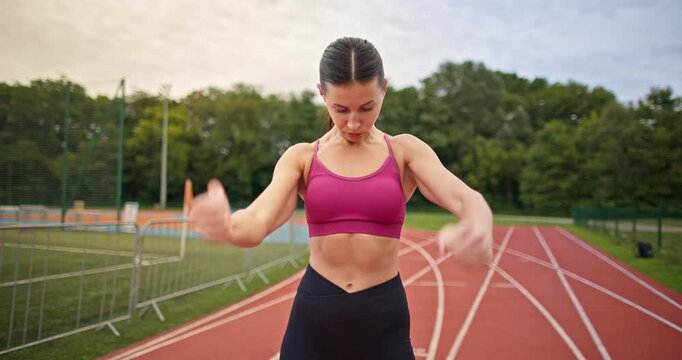 Young athletic woman in sportswear warming up and doing exercises on the stadium running track in the evening at sunset