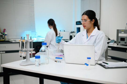 Asian Female Scientist Using Pipette in Modern Research Laboratory with Colleague Working in Background