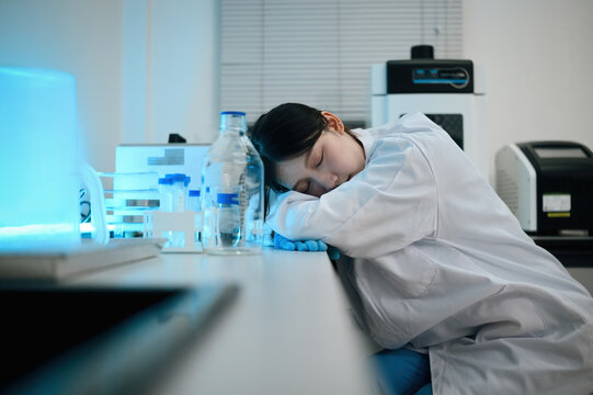 Exhausted Female Scientist Sleeping on Laboratory Bench Surrounded by Glassware and Equipment