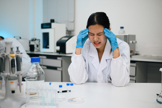 Stressed Female Asian Scientist with Headache in Laboratory Holding Head in Frustration