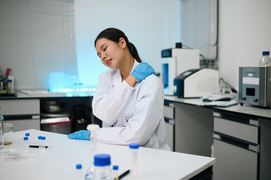 Asian Female Scientist Experiencing Neck Pain in Laboratory While Wearing White Lab Coat and Blue Gloves