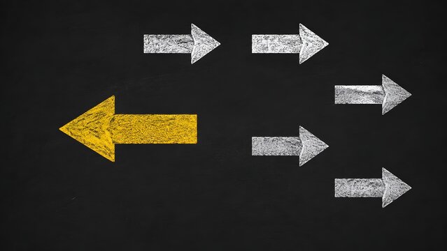 Yellow chalk arrow pointing in the opposite direction of white arrows on a blackboard. Concept of unique business strategy and individuality.
