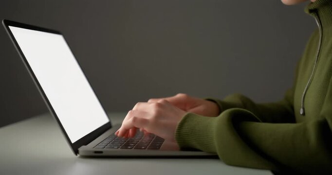 Hands in green hoodie typing on laptop keyboard at workstation setup