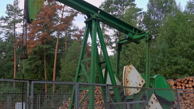 Oil pump jack extracting crude oil from a well in a forest. Fossil fuel production and drilling in northern germany