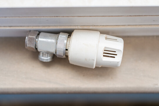 Close-up of a radiator thermostat and heating pipe connection inside a home, representing residential heating, energy efficiency, maintenance and renovation.