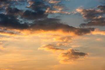 Fototapeta premium Beautiful evening sky during sunset with dramatic golden light illuminating soft cumulus clouds beneath dark stormy cloud formations.