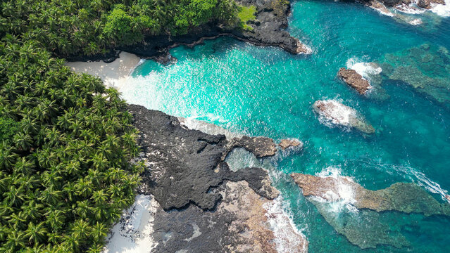Aerial view from Bateria beach at Ilheu das Rolas framed by dense rainforest and volcanic rock formations, with turquoise waters and one of the island's most secluded coastal hideaways.S&atilde;o Tom&eacute;
