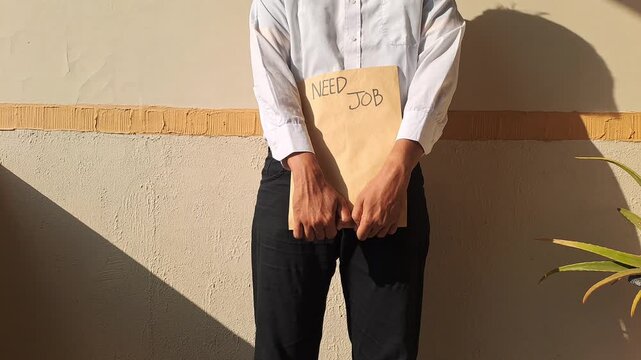 A job seeker in a white shirt gesturing toward a brown envelope with a handwritten need job text. Unemployment, career, and hiring stock video footage.
