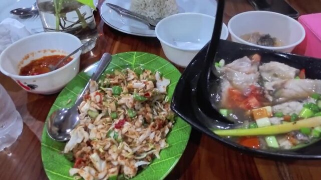 A vibrant dining scene featuring fish soup, rice, chili sauce, and mixed vegetable salad served on a wooden table with colorful textures and flavors.
