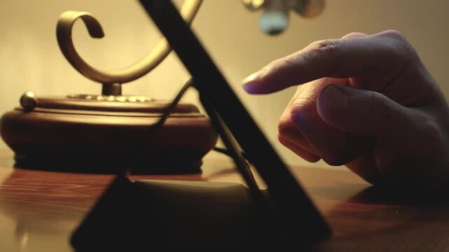 은은한 조명 아래 테이블에 놓인 태블릿 화면을 손으로 가리키며 조작하는 모습