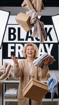Joyful middle aged white woman throws clothing and boxes in the air in a retail store Black Friday