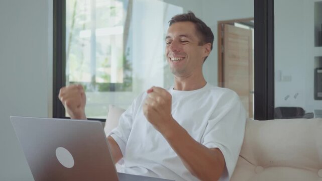 online success man using laptop celebrating achievement and good results at home office. online success concept showing digital work victory excitement and remote productivity lifestyle