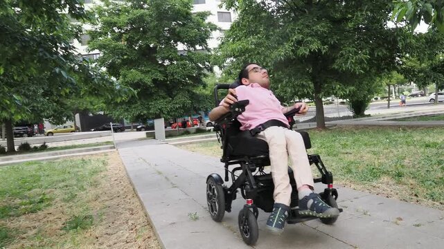 Disabled young man driving an electric wheelchair in a public park