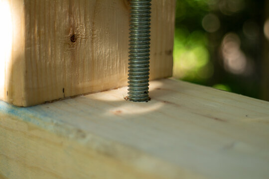 Close-up of a threaded metal bolt inserted through a wooden construction beam