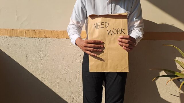 A job seeker holding a brown envelope with a handwritten need work text and gesturing. Unemployment, career, and recruitment stock video footage.