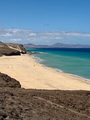Fototapeta premium Canary Islands. Coastal landscape featuring a sandy beach and turquoise waters, with distant mountains visible under a clear blue sky