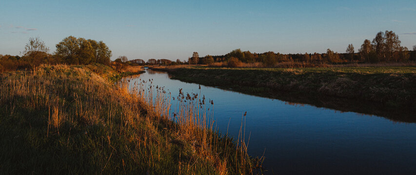 Golden Hour Sunset River Reflecting Blue Sky Over Rural Landscape with Dry Grass Fields