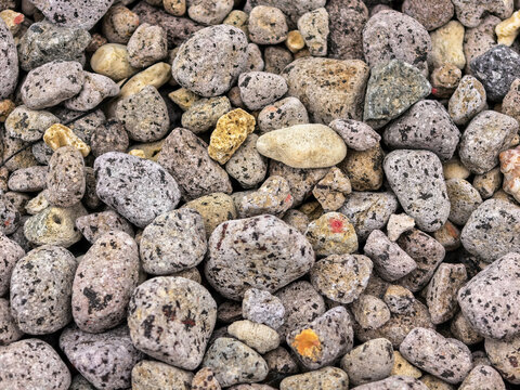 Close-up macro photo of a dense texture of small, weathered grey and speckled beach pebbles and stones.
