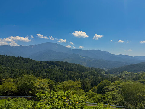 Scenic panoramic view of mountain ranges and lush green forest along Nakasendo trail under blue sky in Japan