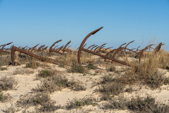 Row of large, corroded ship anchors partially buried in the sand on Praia do Barril, creating a striking landscape
