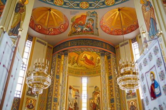 Spacious church interior decorated with colorful frescoes, icons, golden chandeliers and intricate religious ornaments.