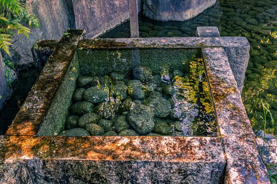 Close-up of clear water and river stones inside a stone well frame at Mejiro Garden May 2024