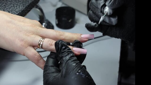 Close-up of a nail technician shaping an artificial fingernail with an electric nail drill during a professional nail extension treatment.